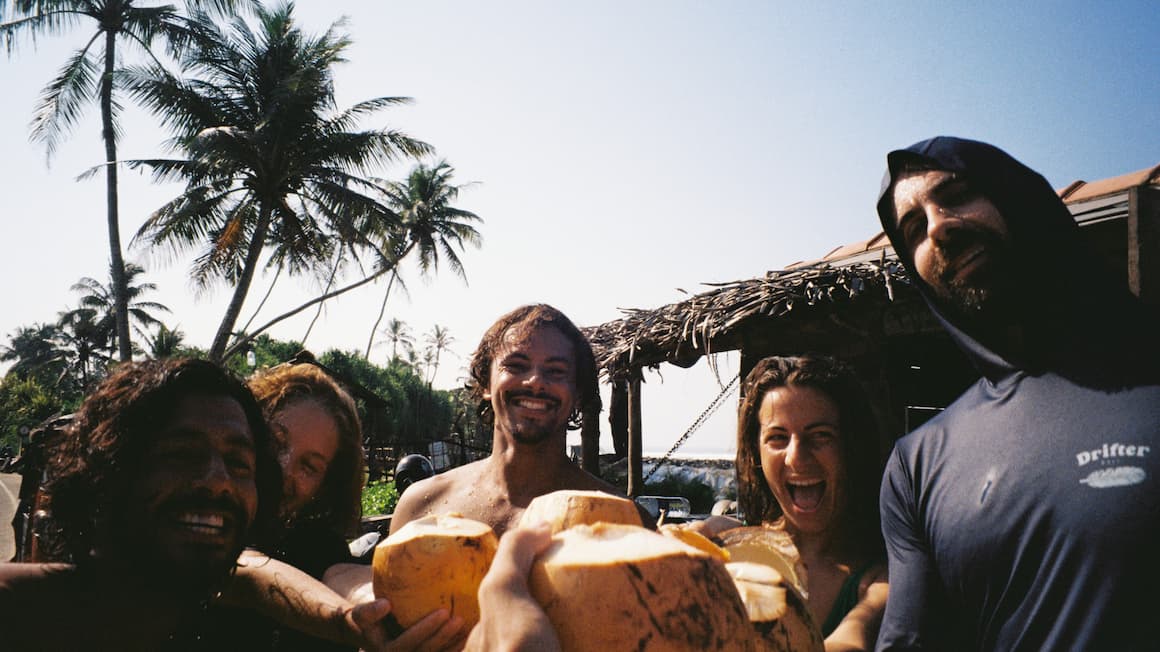 Friends sharing fresh coconuts under palm trees near Midigama, Sri Lanka